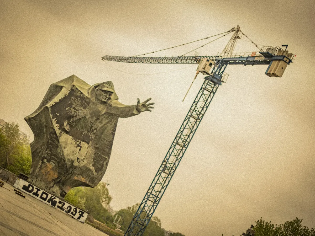 Monumental stone figure reaching toward a construction crane